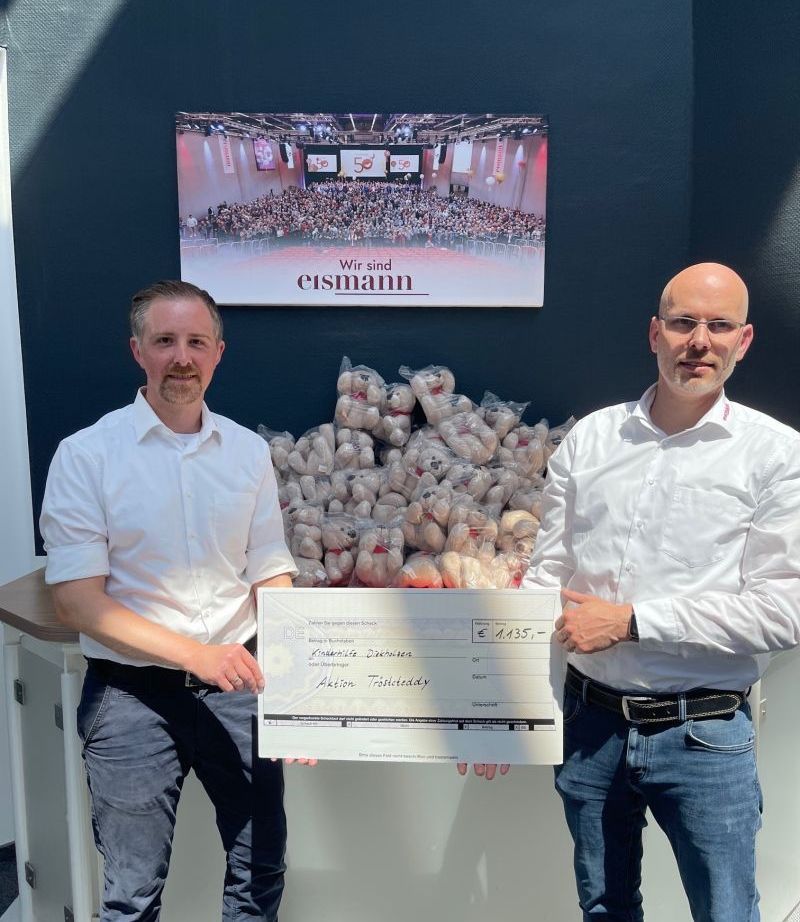 Mitarbeiter mit dem Check in der Hand und den Teddys im Hintergrund